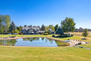 Une grande maison avec un étang au premier plan, entourée d’une pelouse bien entretenue et d’arbres.