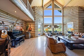 Ein großzügiges Blockhaus-Interieur mit einer imposanten Treppe, einem Klavier und Blick ins Freie.