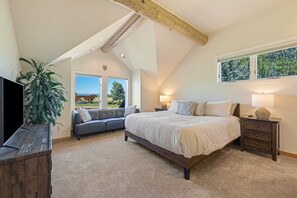 Ein Schlafzimmer mit einem großen Bett, einer Sitzecke inklusive Sofa, einem Fernseher und einem Fenster mit Blick auf Bäume.