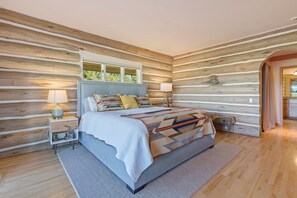 Camera da letto in stile baita con un letto, lampade da comodino e vista sulla natura.