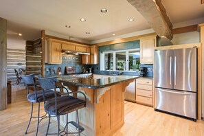 Eine moderne Küche mit Holzausstattung, einem Edelstahlkühlschrank und einer zentralen Kochinsel mit Barhocker.