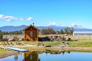 Eine Holzjagdhaus mit einer kleinen Veranda, blauem Himmel und Bergen im Hintergrund.