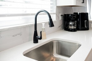 Eine Küchenspüle mit modernem Wasserhahn, einem Seifenspender und einer Kaffeemaschine auf der Arbeitsfläche.