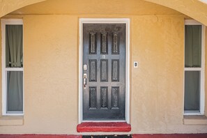 A door with a numeric keypad lock, flanked by windows with curtains, and a red step leading to the entrance. - Paradise by the Gulf unit B-3 br/2 ba duplex close to beach (Indian Rocks Beach)