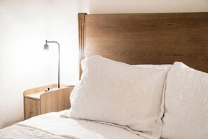 A neatly made bed with a wooden headboard, a bedside table with a lamp, and a wall-mounted light fixture. - Paradise by the Gulf unit B-3 br/2 ba duplex close to beach (Indian Rocks Beach)