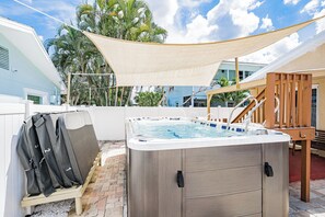 Ein Whirlpool mit Holzterrasse und Sonnensegel, umgeben von einem weißen Zaun und Palmen.