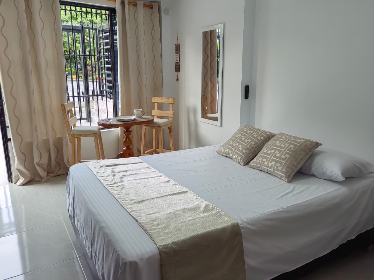 Een slaapkamer met een bed, een stoel, een tafel en een raam met gordijnen.