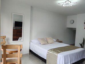 A bedroom with a bed, a chair, a desk, a mirror, and a clock on the wall.