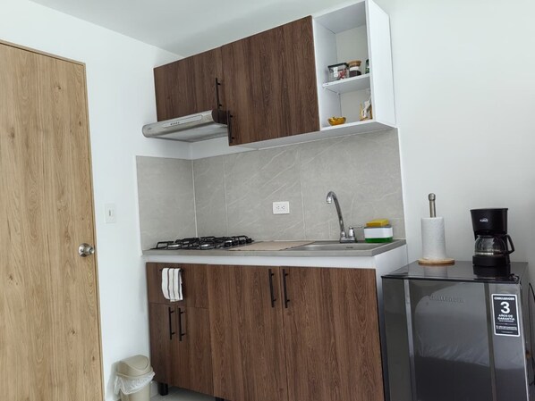 A compact kitchen with a gas stove, a coffee maker, and a refrigerator.