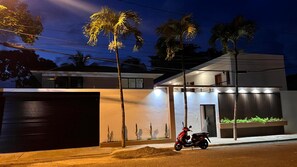 A modern building with a gated entrance, a red scooter parked outside, and a well-lit facade. - Artiora Spacious 10-bedroom Villa with Large Jacuzzi & Pool (Sosúa)
