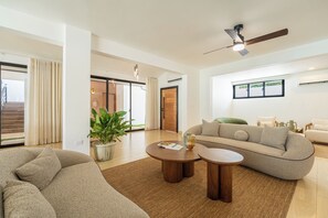 A spacious living room with a sofa, two coffee tables, a ceiling fan, and a large window. - Artiora Spacious 10-bedroom Villa with Large Jacuzzi & Pool (Sosúa)