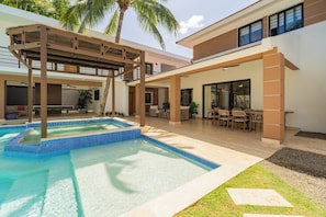 Un área de piscina moderna al aire libre con una pérgola, asientos y un patio cubierto.