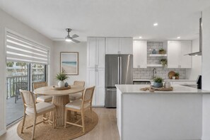 A modern kitchen with white cabinetry, a stainless steel refrigerator, and a dining area with a round table and chairs. -  55+ Gated Waterfront community Condo w/ Dock, Pool, and laundry on site (St. Petersburg)