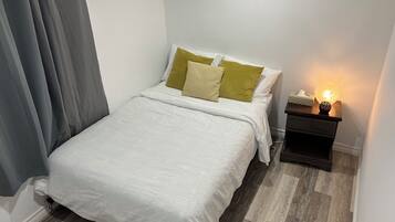A neatly made bed with a white duvet, a bedside table with a lamp, and a wooden floor.