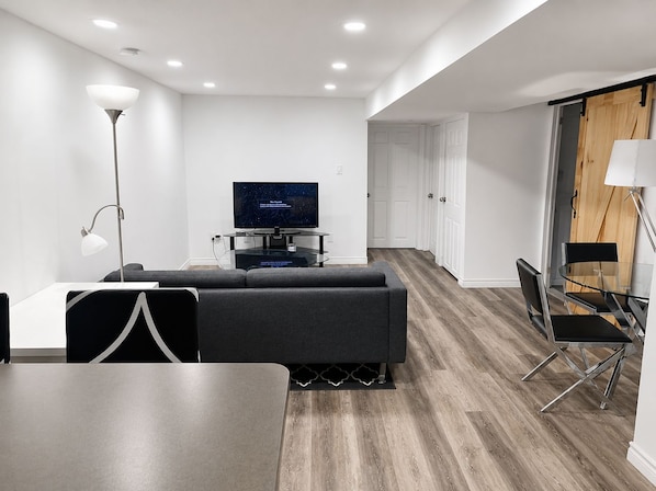 A modern living room with a flat-screen TV, a sofa, a dining table, and a glass coffee table.