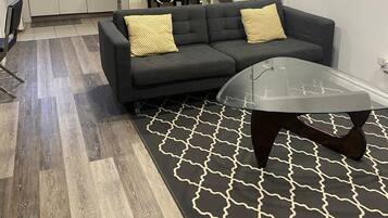 A modern living room with a sectional sofa, a glass coffee table, and a patterned rug.