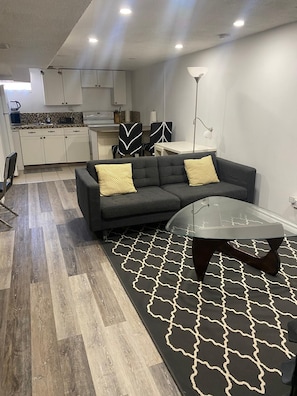 Ein modernes Wohnzimmer mit einem Ecksofa, einem Glastisch und einem gemusterten Teppich.