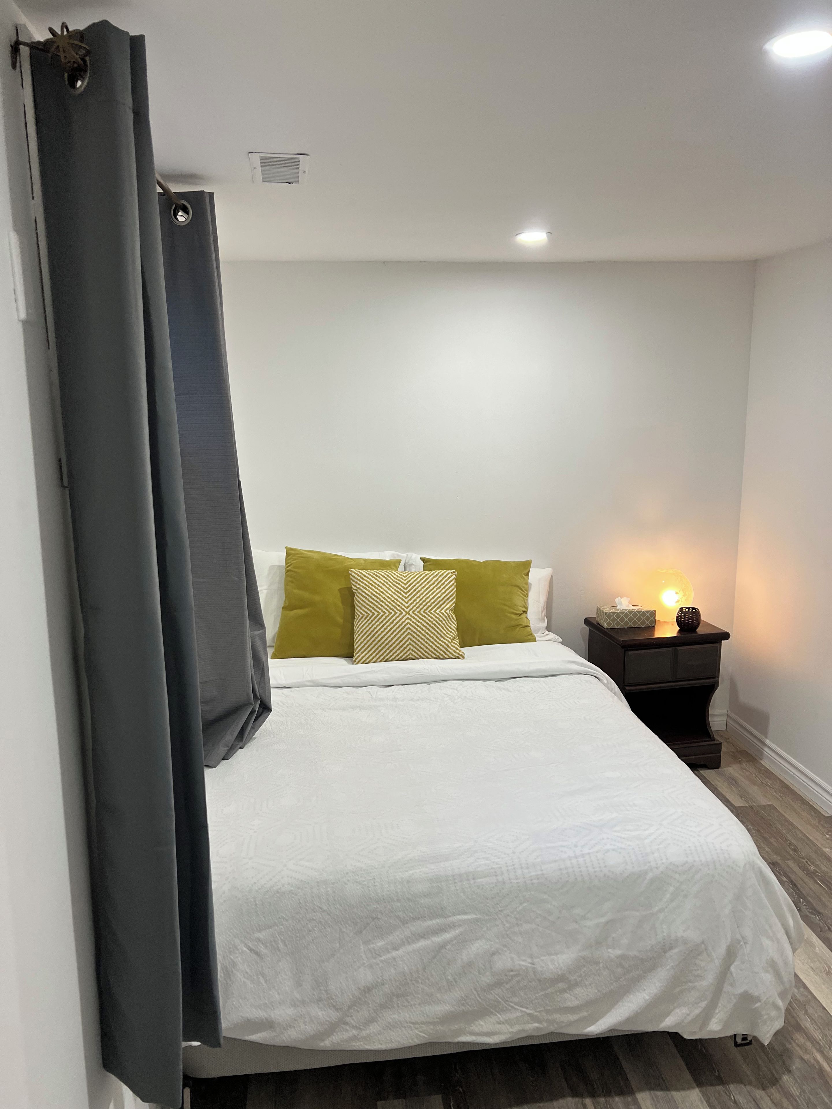 A bedroom with a bed, a nightstand with a lamp, and a window with curtains.