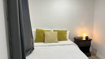 A bedroom with a bed, a nightstand with a lamp, and a window with curtains.