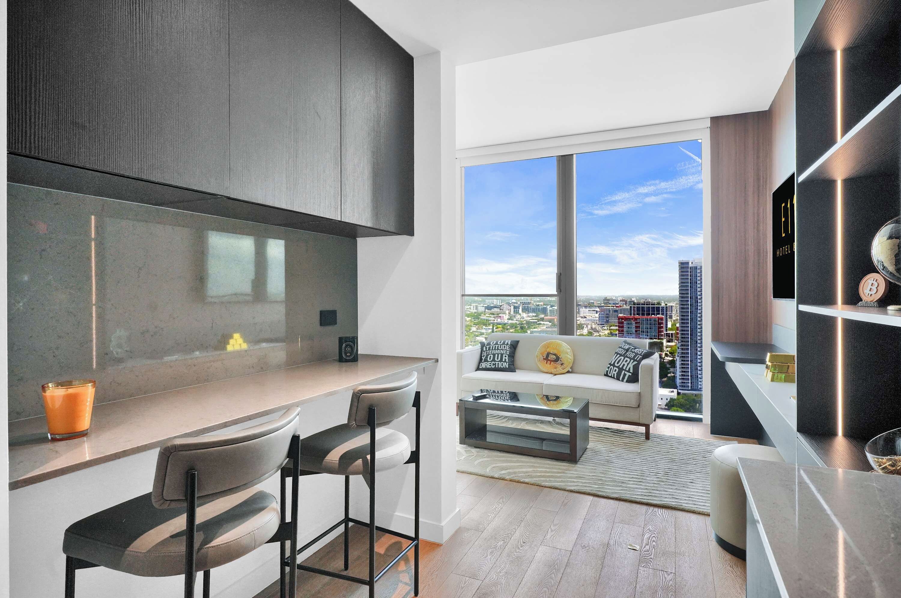 A modern kitchen with a large window, a dining area with a sofa and chairs, and a view of the cityscape.