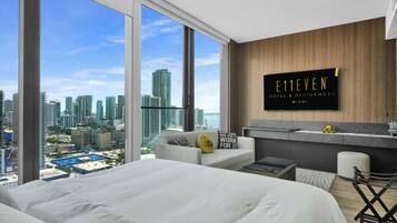 A modern hotel room with a large bed, a seating area, and a city view.