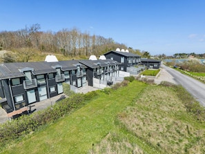 A row of modern, dark-colored houses with large windows and balconies, situated on a grassy slope with a road and trees in the background. - 4 Star Holiday Home in Martofte (Martofte)