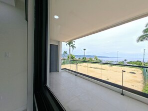 A balcony with a view of a beach and palm trees. - New/Top Road/Gated/AC/Wi-fi/TV/Pool/Sea view/Gym (Montego Bay)