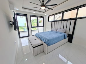 Ein modernes Schlafzimmer mit einem Bett, einem Deckenventilator, einer Bank und großen Fenstern.