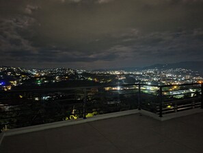 Ein nächtlicher Blick auf eine Stadtlandschaft von einem Balkon mit Geländer.