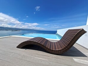 Ein Korbsessel auf einer Holzterrasse mit Blick auf ein Schwimmbecken und eine Fernsicht auf das Meer und das Land.