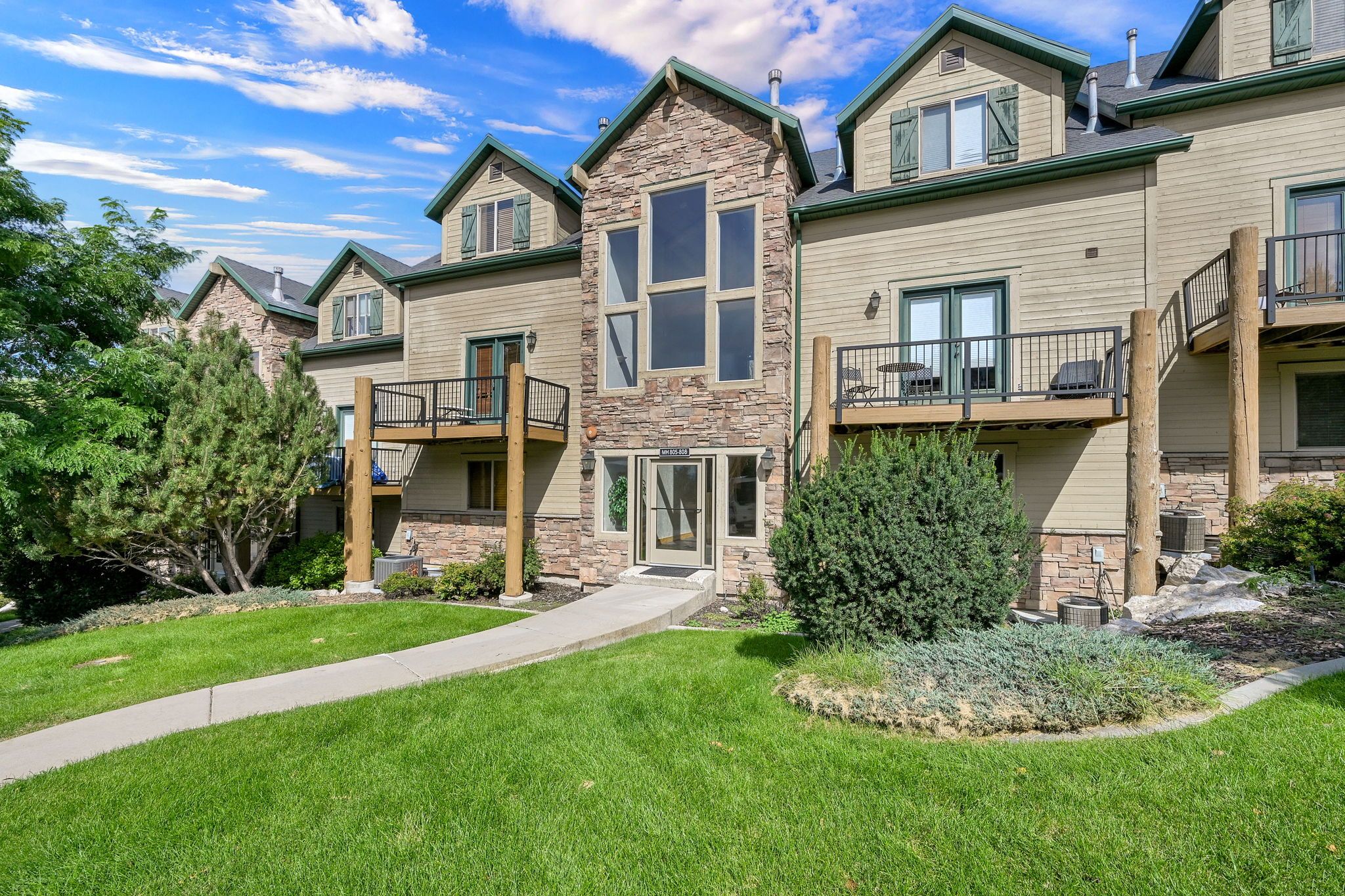 A multi-story residential building with a stone facade, a central entrance, and a balcony with outdoor furniture.