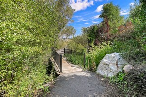Eine Holzbrücke über einen Kiesweg, umgeben von dichtem Grün.