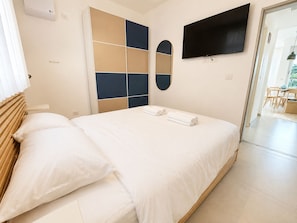 Habitación de hotel con cama, armario, televisión y baño visible a través de una puerta abierta.