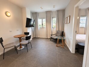 Une chambre moderne équipée d’un téléviseur à écran plat, d’une table de salle à manger ronde, de deux chaises, d’une table basse en verre, d’un canapé et d’un lit.