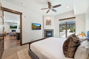 Ein modernes Schlafzimmer mit einem großen Bett, einem Kamin, einem Deckenventilator und Blick ins Freie.