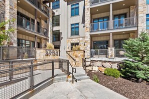 A multi-story building with a stone facade, balconies, and a gated entrance. - Luxury 2BR Canyons Village Condo: Walk to Lift, Pool, Hot Tub & Viking Kitchen (Park City)