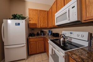A kitchen with wooden cabinets, a white refrigerator, a microwave, a stove, and a kettle. - 3BR Disney Gataway/Bahama Bay Resort/Davenport FL (Davenport)
