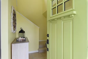 A hallway with a light green door, a white door, and a staircase leading to an upper floor. - Bay Breeze Chincoteague | Bay Views + Modern Comfort! (Chincoteague Island)