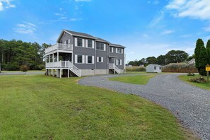 A two-story house with a covered porch and a gravel driveway. - Bay Breeze Chincoteague | Bay Views + Modern Comfort! (Chincoteague Island)