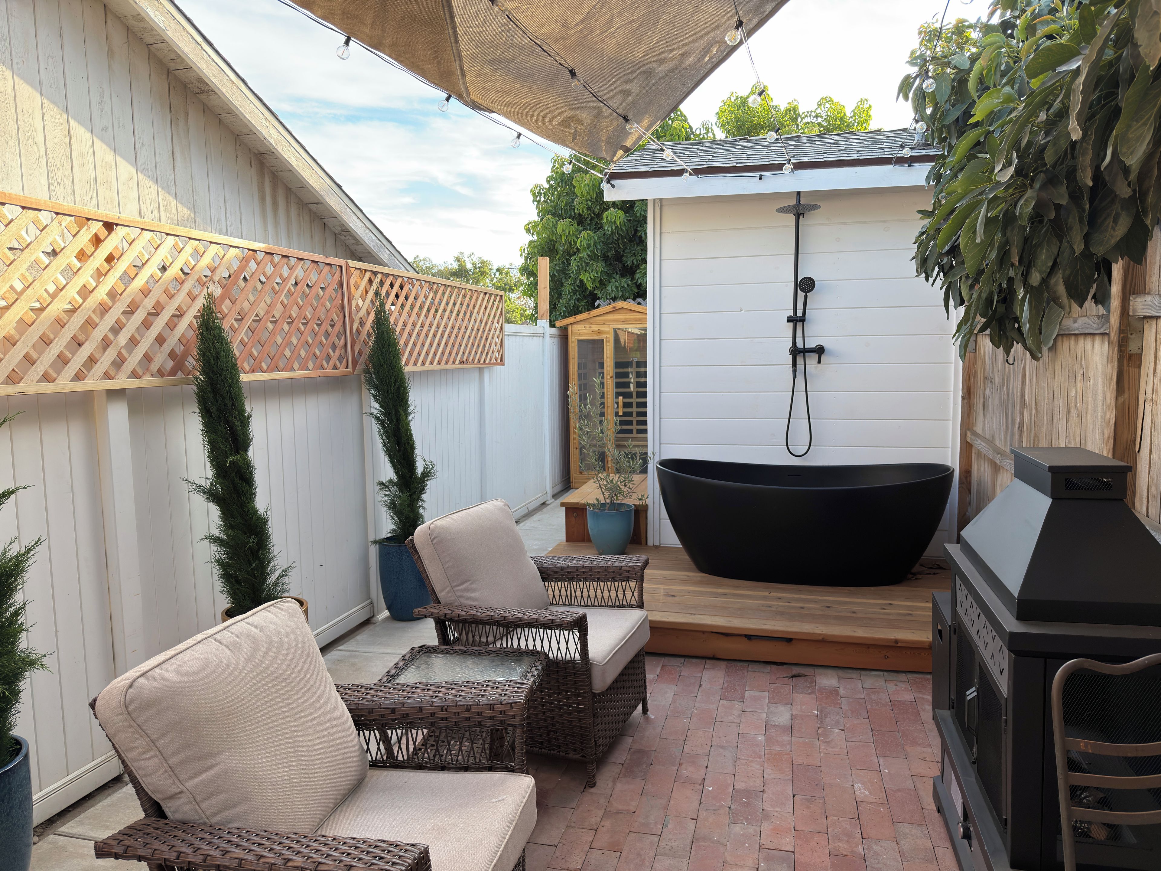 Un espacio de patio con mobiliario de mimbre, una bañera de hidromasaje negra y una parrilla de barbacoa.