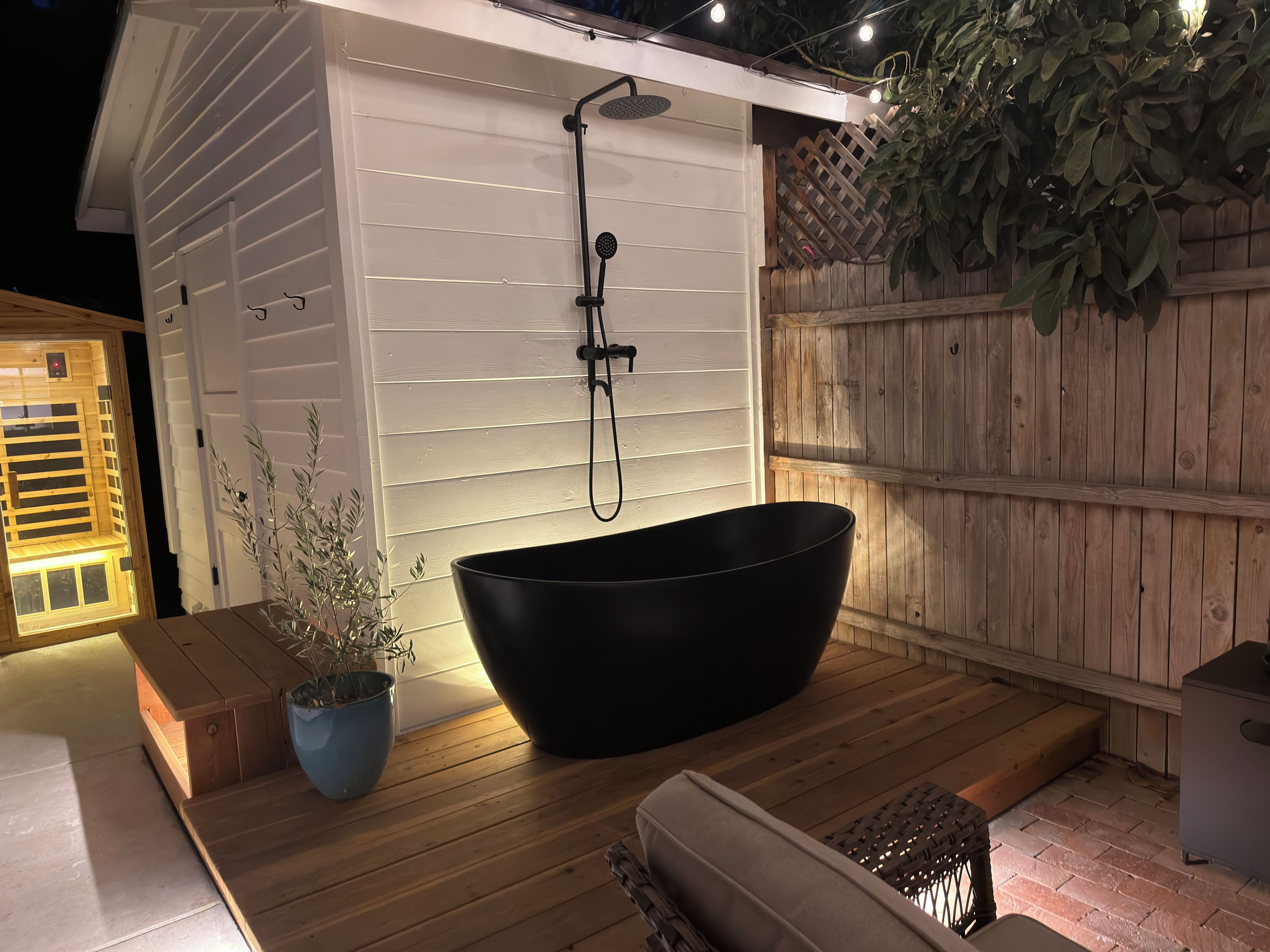 Un'area benessere con una grande vasca da bagno nera, un pontile in legno e un edificio bianco con recinzione in legno.