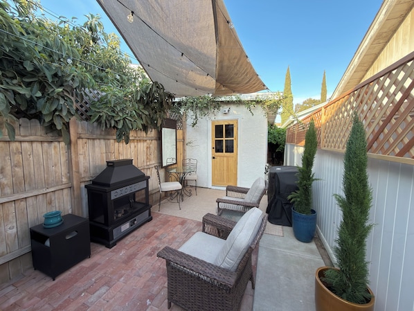 Eine Terrassenfläche mit Grill, Korbmöbeln und einem Holzzaun.