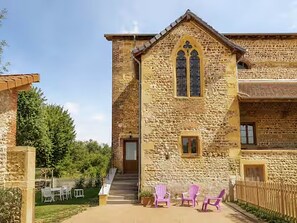 A stone building with a gabled roof and a central entrance. There are outdoor chairs and a small table in front of the building. - Chapelle Valvert - heated pool, sleeps 12 (Chandon)