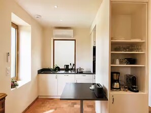 Une cuisine compacte avec des meubles blancs, un plan de travail noir et un appareil à café intégré.
