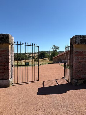 A gated entrance with a clear sky, a dirt path leading to a building, and a natural landscape in the background. - Chapelle Valvert - heated pool, sleeps 12 (Chandon)