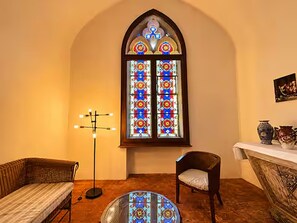 A room with a large stained glass window, a floor lamp, a chair, and a small table with decorative items. - Chapelle Valvert - heated pool, sleeps 12 (Chandon)