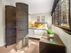 A bedroom with a bed, a nightstand, a potted plant, and a window with a view of trees. - Ski Access, Bonus Room, Parking Garage, Hot Tub, and Prime Location! (Park City)