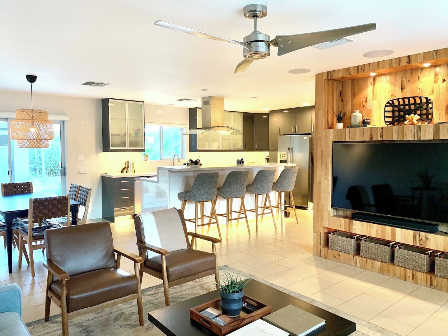A modern living room with a fireplace, a dining area with a table and chairs, and a kitchen with a bar area.