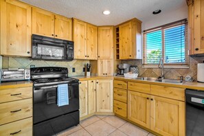 A kitchen with wooden cabinets, a black stove, a microwave, and a window with blinds. - Pikes Peak Retreat | Hot Tub, Firepit + Pets (Colorado Springs)