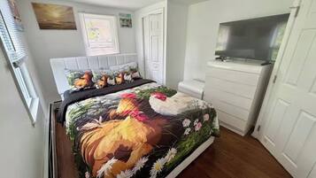 A bedroom with a bed, a TV, a white wardrobe, and a window with blinds.